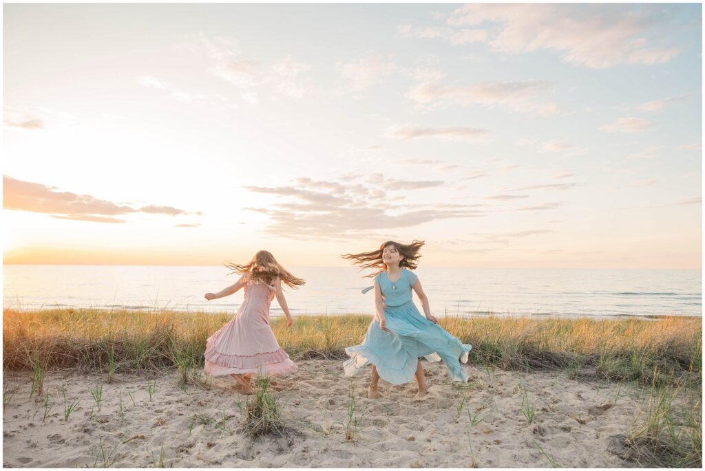 Indiana dunes family photos: two young sisters dance in the sand by Lake Michigan