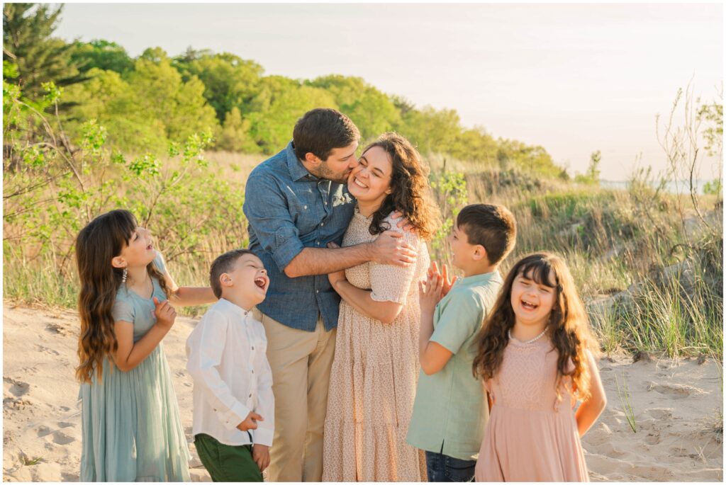 Indiana dunes family photos: a family of 6 laughing together as Dad gives Mom a kiss on the cheek