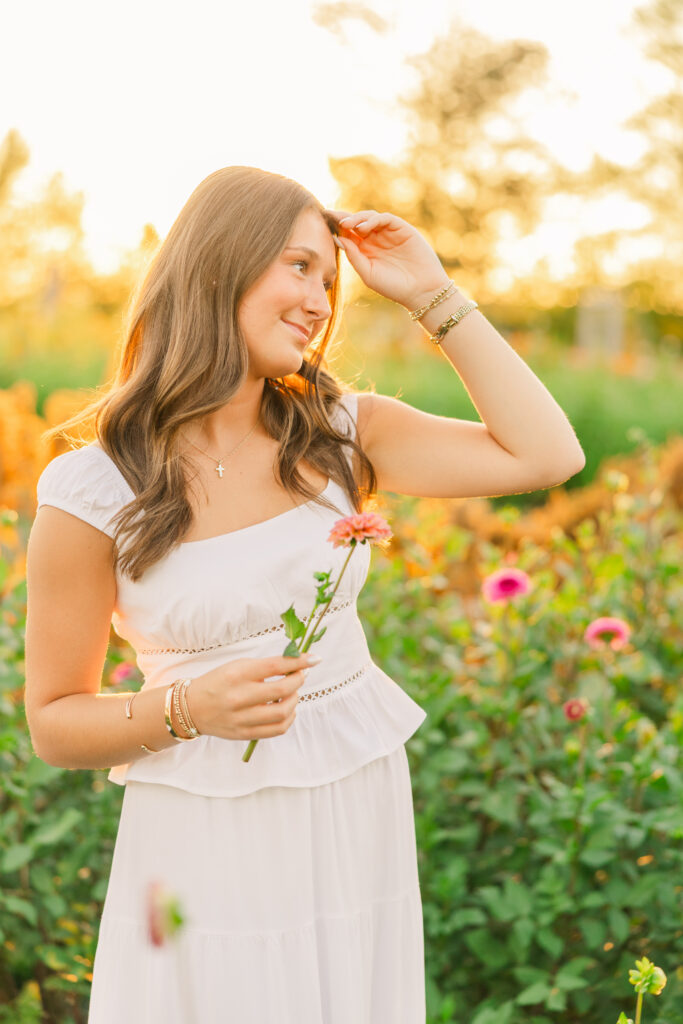 Glowy senior photo of girl in white dress holding a flower at a Sweet Pea Flower Farm in Noblesville, Indiana