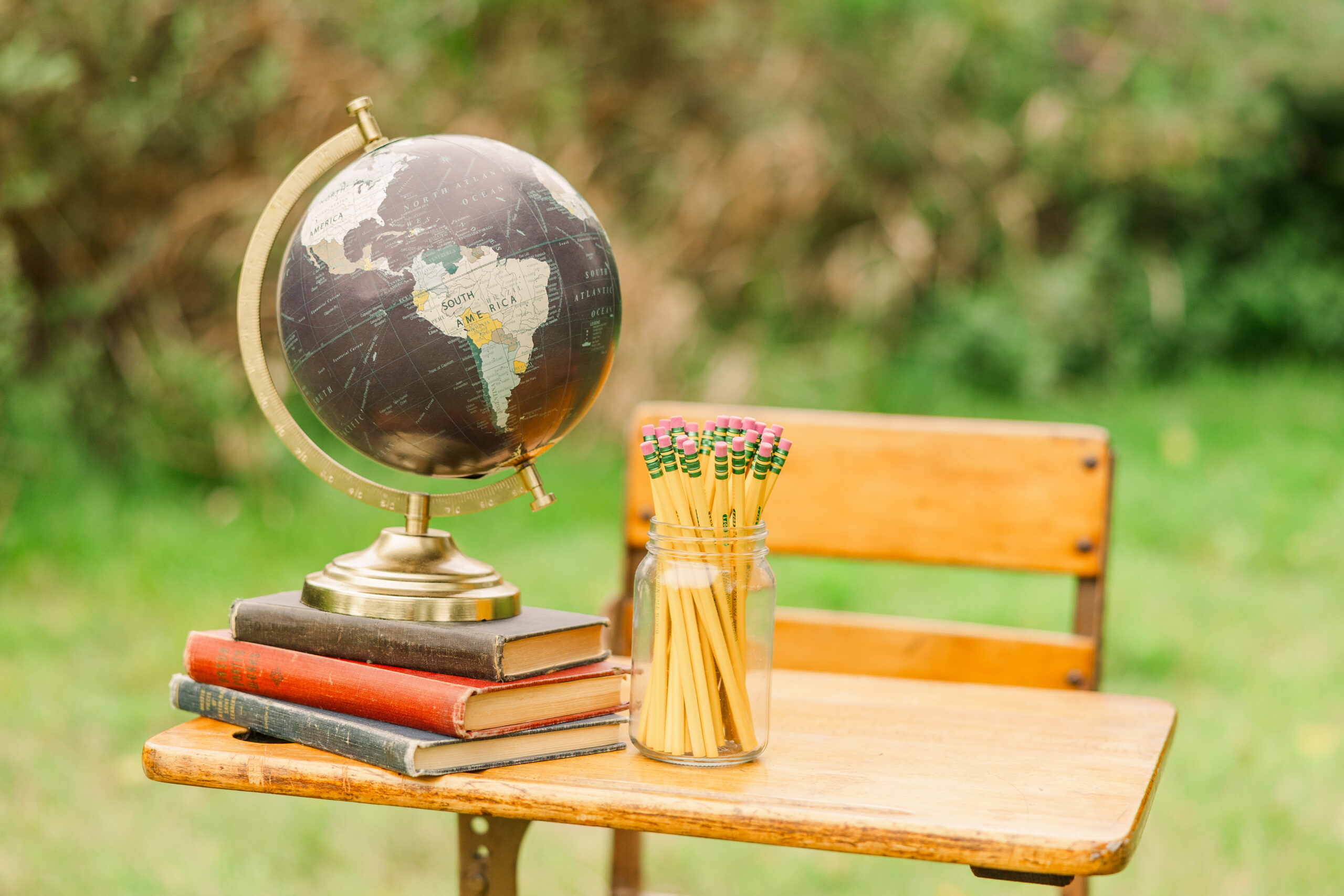A stack of old books, a jar of pencils and a globe sitting on top of an antique desk.