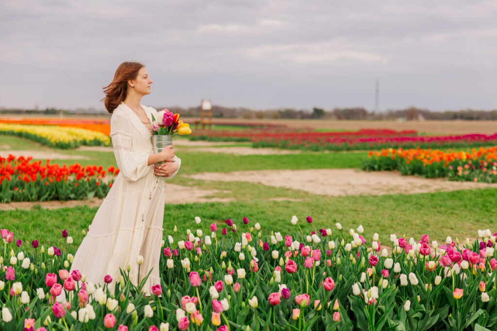 a high school senior holding a bucket of vibrant tulips standing in a tulip field