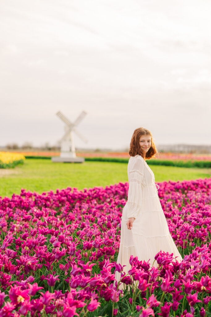 girl in rows of magenta tulips in a cream flowy dress with a windmill in the background