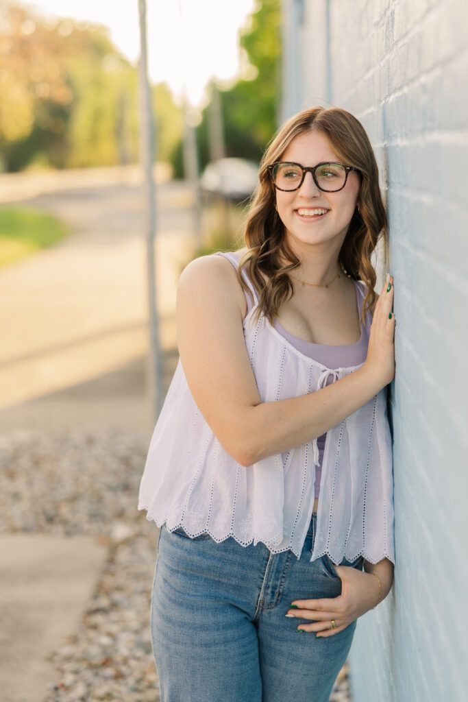 Senior girl leaning against a blue brick wall in a senior photo session.